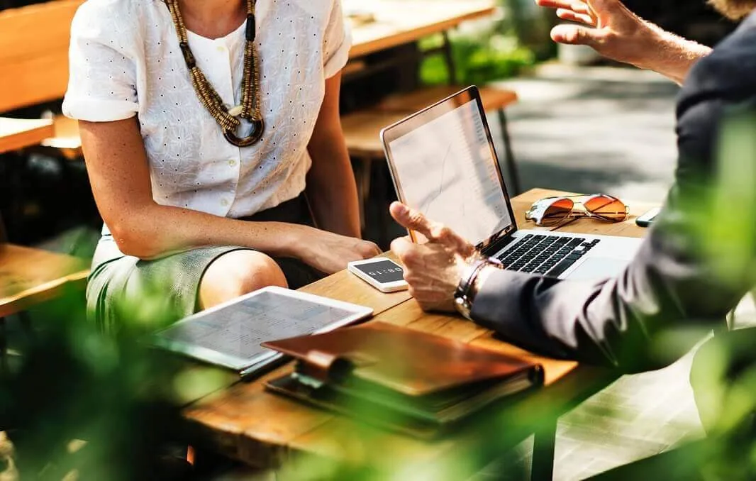 absprache_strategie Strategiegespräch zweier Personen mit Laptop und Tablet an einem Tisch im Grünen