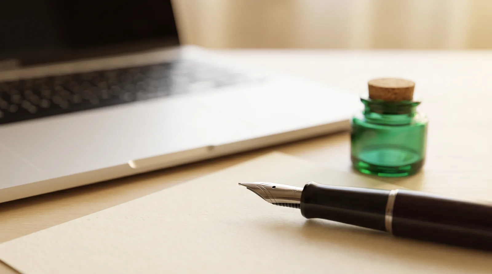 seo-texte-schreiben-lassen Füllfederhalter auf Papier neben grünem Tintenfass und Laptop, Symbol für SEO-Texte schreiben lassen