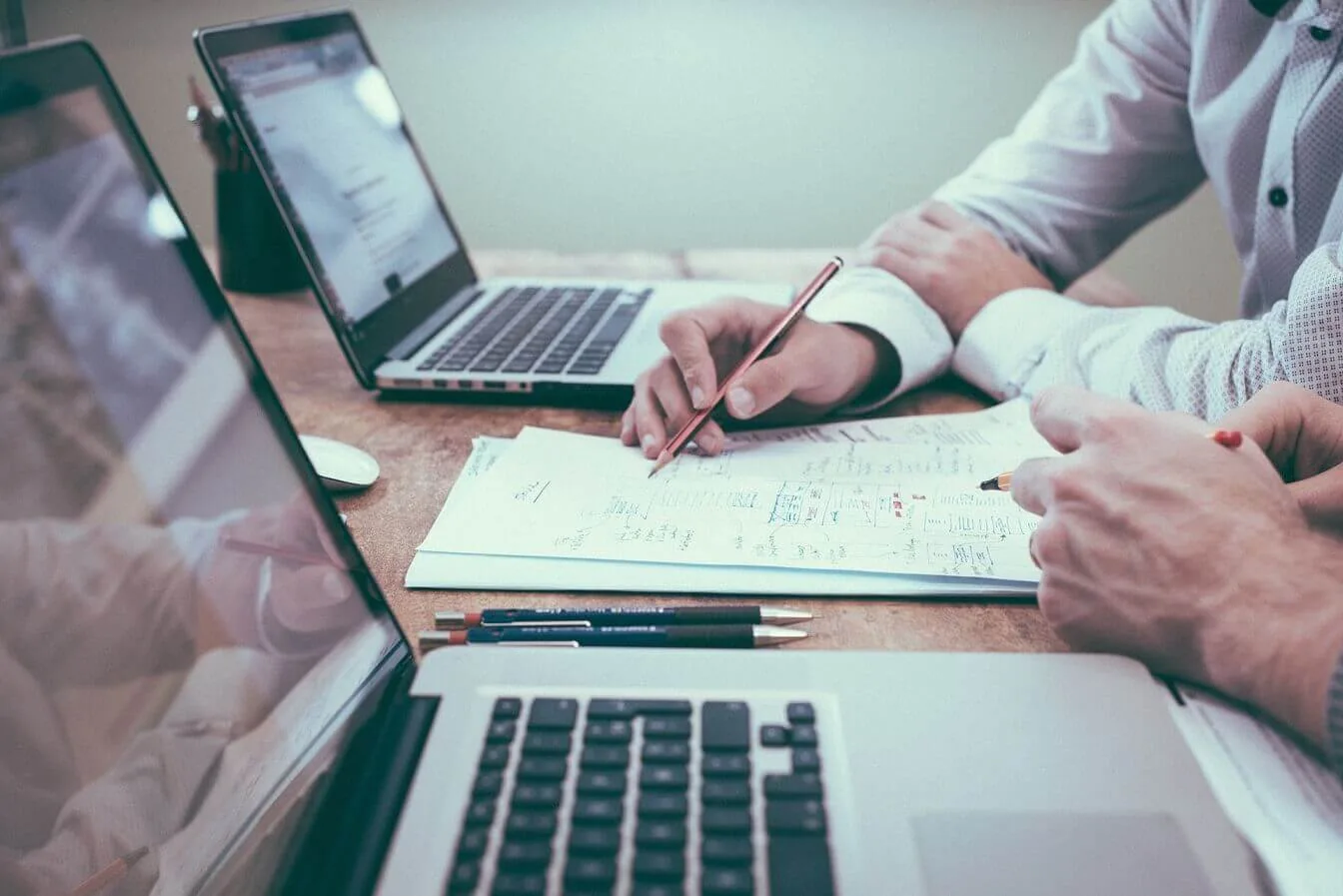 Zwei Personen besprechen handgezeichnete Skizzen und Diagramme zwischen zwei Laptops, SEO-Spezialist bei der Arbeit